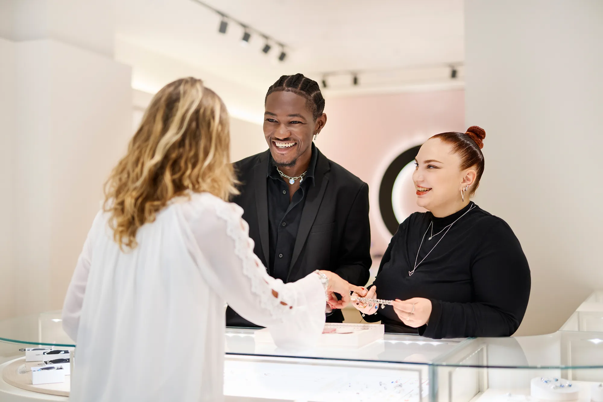 Jewelry store staff smiling and assisting a customer with a bracelet at a counter