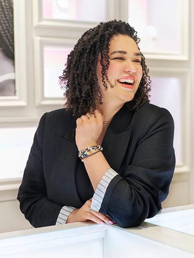 Leah Buckman smiles and laughs wearing a black blazer and a charm bracelet