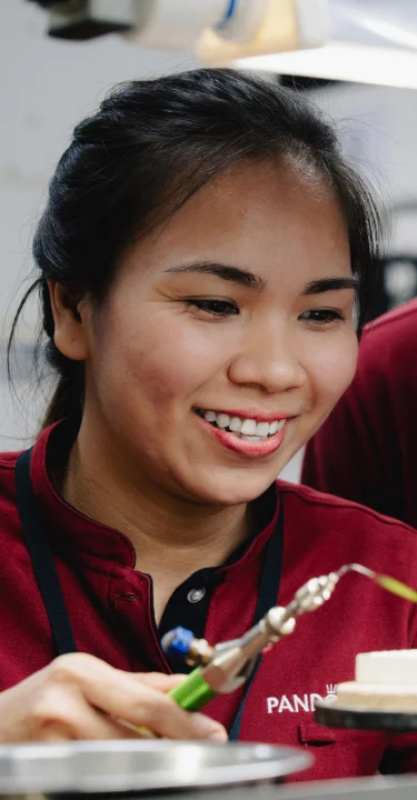 Two women in red shirts crafting with small pieces under bright lights