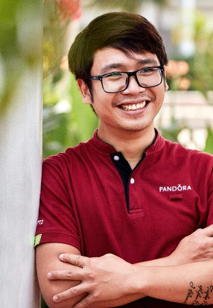 A smiling Pandora employee hands a shopping bag to a customer in a jewelry store.