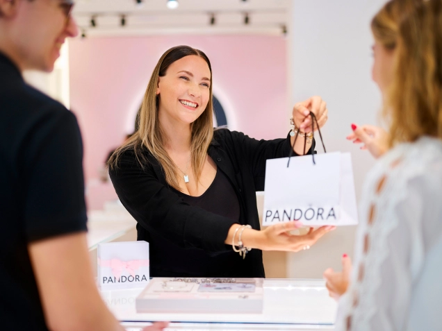 A man and two women examine jewelry at a Pandora store.