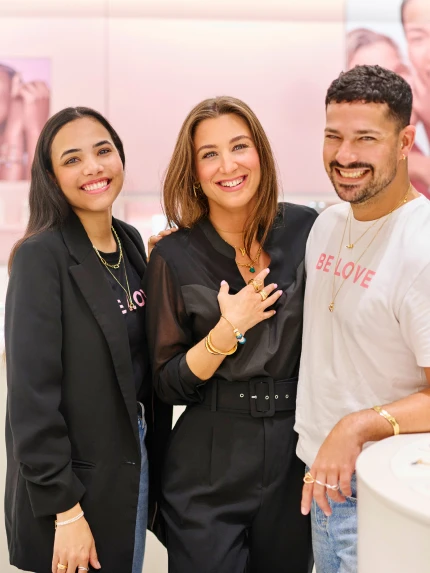Three people smiling together indoors with a pink background