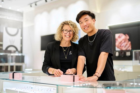 Four smiling staff members in a Disney x Pandora store stand behind a glass display case showing Pandora jewelry.
