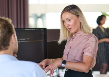 Two professionals discuss code on a computer screen in a modern office setting